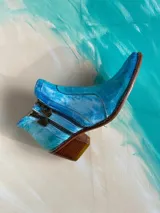 Bota corta de cuero vacuno pintada a mano en tonalidades turquesa y celeste, con taco cuadrado de madera, doble cierre lateral con tiradores metálicos personalizados y punta fina.