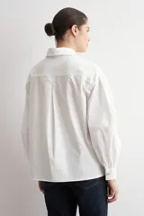 Camisa de corte oversized, color blanco, con cuello clásico, cierre frontal de botones y mangas largas.
