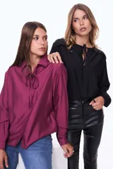 Camisa negra de corte clásico con cuello camisero y detalle de lazo ajustable en el cuello. Presenta cierre frontal con botones y mangas largas con puños abotonados.