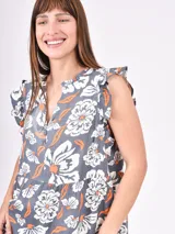Vestido corto de corte holgado con estampado floral en tonos blancos y naranjas sobre base gris oscuro. Presenta escote en V, mangas con volados y diseño escalonado.