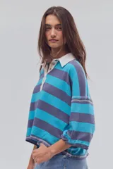 Remera tipo polo de algodón, de calce oversize, con diseño a rayas en tonos azul y celeste, cuello clásico blanco, botonadura corta, hombros caídos y mangas cortas.