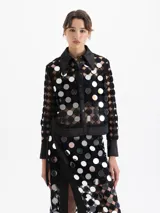 Camisa de manga larga negra, confeccionada en guipur con apliques circulares de espejo. Posee cuello y puños de tela lisa negra, cierre frontal con broches snap forrados y un top interno negro.