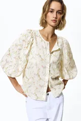 Blusa en tejido liviano de mezcla de lino, de color blanco con estampado floreado. Cuenta con cuello redondo, cierre frontal de botones y mangas globo tres cuartos con puños elásticos.