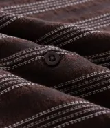 Camisa de manga corta con cuello solapa y cierre frontal de botones. Presenta un diseño de rayas verticales con textura jacquard en tonos marrones.