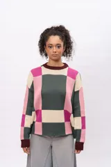 Buzo de tejido de punto con diseño geométrico de cuadros en tonos verde oscuro, rosa y crema. Presenta cuello redondo, puños y ruedo en color bordó, con mangas largas y corte holgado.