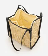 Cartera tipo shopper confeccionada en paja trenzada de color beige con detalles en negro, asas de hombro de poliuretano y compartimento interior con cierre de cordón ajustable.