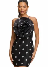 Vestido corto negro con estampado de lunares blancos, presenta un diseño de escote halter con una gran aplicación floral tridimensional en el pecho.