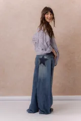 Jean wide leg de tiro alto y lavado azul desgastado, con cinco bolsillos y detalles de estrellas en denim oscuro con tachas metálicas en los bolsillos traseros.