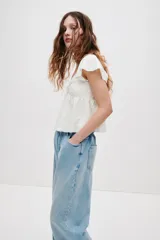 Blusa corta blanca en punto pointelle con textura, escote corazón, mangas cortas circulares, detalle cut-out con cordón de ajuste en el busto y diseño acampanado con costura fruncida.