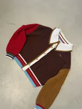 Cardigan de punto con diseño color block, cuello estilo polo en color rosado con borde rojo, cierre frontal con botones, manga derecha en verde oliva y manga izquierda en rojo, con puños y ruedo acanalados a rayas multicolor.