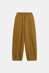 Pantalón de tiro medio y pierna ancha, confeccionado en hilatura con mezcla de algodón. Cuenta con cintura elástica con cordón de ajuste, bolsillos laterales ocultos y bajo abullonado con pliegues frontales.