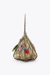 Bolso rígido con estructura metálica dorada y forro interior de tela color beige ajustable con lazada. Decorado con charms colgantes de diferentes motivos y asa superior rígida.