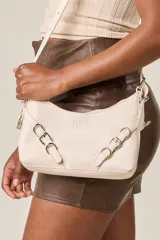 Bandolera color crema con correa fina regulable, cierre superior y herrajes metálicos plateados con forma de hebilla.