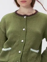 Cardigan de algodón grueso color rojo, con cuello redondo, cierre frontal de botones grandes y bolsillos cuadrados en el frente. Presenta detalles de pelo sintético en el cuello y los bolsillos, y logo bordado en uno de los bolsillos.