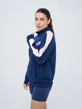 Buzo de felpa azul marino con medio cierre, cuello alto, bandas laterales en tono rosado y bolsillo frontal tipo canguro. Presenta el logo de Umbro y el escudo del Club Nacional de Football bordados.