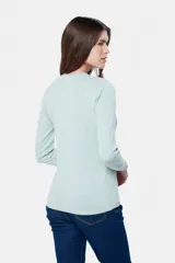 Buzo tejido en hilo de algodón color beige, con cuello redondo y manga larga. Presenta un corte clásico y un pequeño detalle metálico en la parte inferior izquierda.