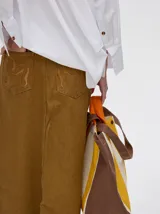 Pollera midi de denim color marrón, de tiro medio y corte recto. Presenta cierre frontal con botones metálicos a la vista y un tajo central en el ruedo con terminación deshilachada.