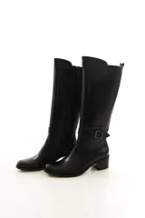 Bota de caña alta confeccionada en cuero legítimo color marrón, con diseño clásico, costuras visibles y una delicada tira con hebilla lateral. Cuenta con cierre lateral interno y taco medio ancho.