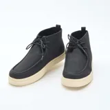 Zapatos tipo chukka de corte casual, con capellada en color negro y suela de goma en tono crema. Presentan cierre mediante cordones y una costura distintiva en la puntera.