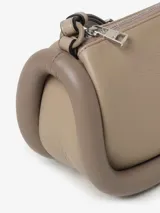 Bolso de hombro color beige, marca JW Anderson, modelo Bumper-12. Confeccionado en cuero con ribetes tubulares acolchados. Tiene correa de hombro ajustable, cierre con cremallera superior y logo estampado en el frente.