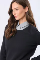 Buzo tejido en hilo de algodón color beige, con cuello redondo y manga larga. Presenta un corte clásico y un pequeño detalle metálico en la parte inferior izquierda.