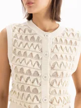Chaleco color beige confeccionado en tejido semiliviano de galga 12, con calce regular, largo hasta la cadera y escote redondo clásico. Su diseño presenta una trama texturada con figuras geométricas.