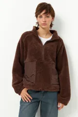 Buzo negro de teddy con cuello alto y cierre de cremallera parcial. Presenta bolsillos de nylon en la parte inferior delantera.