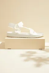 Sandalias planas color blanco, con tiras de tela tipo cinta y cierre ajustable con velcro.