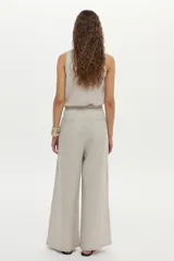 Pantalón de lino color beige, de pierna amplia, con elástico en la cintura, pinzas en el frente y bolsillos laterales y traseros.