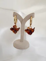 Aros tipo argolla dorada con dije colgante en forma de flor de resina en tonos marrones.