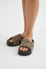 Sandalia plana con plataforma negra y tira ancha de pelo con estampado animal print tipo leopardo, decorada con tachas metálicas en los bordes.