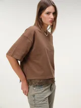 Remera boxy de manga corta marrón, de corte holgado y diseño liso, con detalle de encaje a tono en el borde inferior.