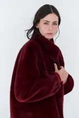Chaqueta de piel sintética en color burdeos, con cuello alto y cierre frontal oculto. Presenta un diseño de corte recto y mangas largas con puños ligeramente ajustados.