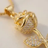 Cadena de acero con baño de oro y dije de bronce con forma de rosa, decorado con circonias incrustadas.