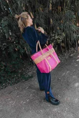 Bolso tipo shopper de lona fucsia con detalles en cuero natural, incluyendo asas, correas verticales y una banda horizontal decorativa con hebilla central. Cuenta con una etiqueta de cuero grabada con la marca Sierra Mora.