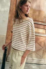 Camiseta de algodón a rayas horizontales en tonos marrones y beige, de corte regular fit, cuello redondo a contraste de color marrón oscuro y mangas largas por debajo del codo. Presenta diseño de bajo asimétrico.