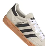 Championes Adidas modelo Handball Spezial, confeccionados en gamuza color beige con las icónicas tres tiras laterales en negro. Presentan suela de goma color caramelo y detalle de talón en negro.