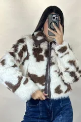Campera corta de piel sintética con estampado de manchas tipo vaca en tonos blanco y marrón. Presenta cuello camisero, cierre frontal con cremallera y detalles en cuero sintético marrón en el cuello y la solapa del cierre.