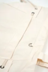 Bolso tipo tote bag color beige con asas superiores de hombro, cordones ajustables a los lados con detalles metálicos y un pequeño anillo frontal.