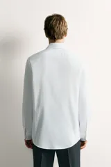 Camisa de corte regular fit color celeste, confeccionada en tejido fácil de planchar. Cuenta con cuello italiano abierto, manga larga con puño abotonado y cierre frontal con botonadura.