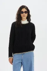 Sweater negro tejido de mohair, con cuello redondo, mangas largas y detalles en hilo blanco en el cuello, los puños y el ruedo.