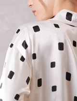 Camisa de satén con estampado de rectángulos negros sobre fondo blanco. Presenta cuello clásico con solapa, cierre frontal con botones metálicos y mangas largas con puños rectos.