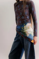 Pañuelo cuadrado de seda con diseño estampado tipo patchwork que combina motivos botánicos, arquitectónicos y geométricos en tonos azules, verdes, ocres y crema, con un borde a rayas multicolor.