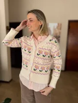 Cárdigan de punto con diseño jacquard floral en tonos rosa, amarillo y verde sobre base color crema. Presenta cuello en V, cierre frontal con botones grandes y detalles de calados en el tejido.