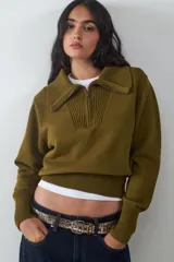 Sweater de punto color verde oliva, con cuello polo y cierre frontal parcial, de manga larga con puños anchos y diseño acanalado en el bajo.