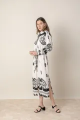 Vestido camisero midi de lino y viscosa color crudo con estampado de palmeras en negro. Tiene cuello camisero, mangas largas con puños y cinturón de la misma tela.