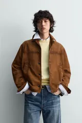 Cazadora de piel con acabado ante color marrón, corte relaxed fit, cuello bowling y manga larga con puño abotonado. Presenta bolsillos de vivo en la cadera y cierre frontal de botonadura.