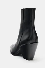 Botín estilo cowboy de piel color negro, con caña baja, acabado en punta y tacón medio en bloque. Cuenta con cierre mediante cremallera lateral.
