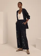 Pantalón de encaje negro con corte recto, tiro alto, cierre frontal con cremallera, dos bolsillos y forro incorporado.