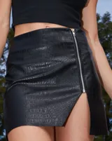 Minifalda negra de ecocuero con textura croco, cierre metálico lateral y tajo en la pierna derecha.